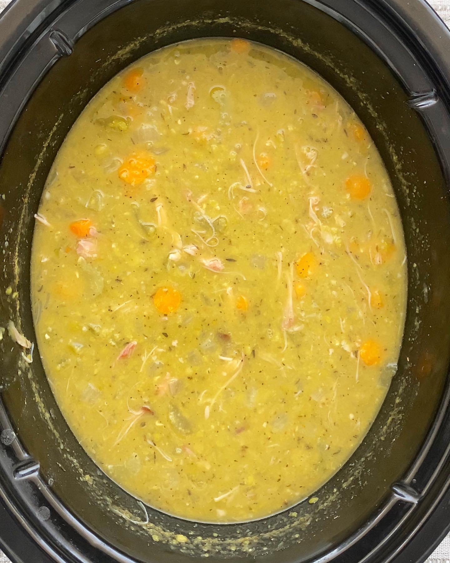 overhead shot of uncooked split pea soup in a black slow cooker with shredded turkey
