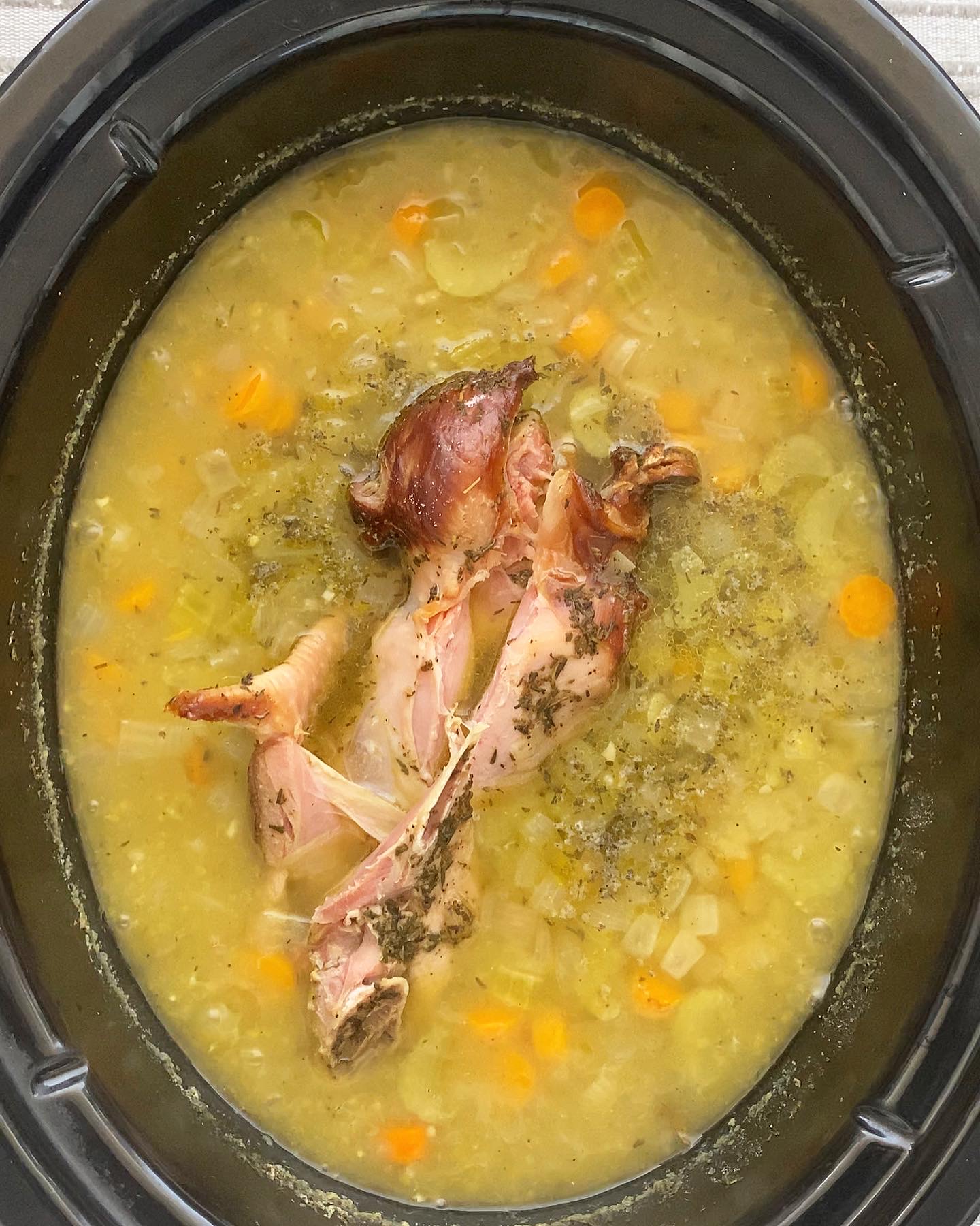 overhead shot of cooked split pea soup in a black slow cooker with a turkey wing