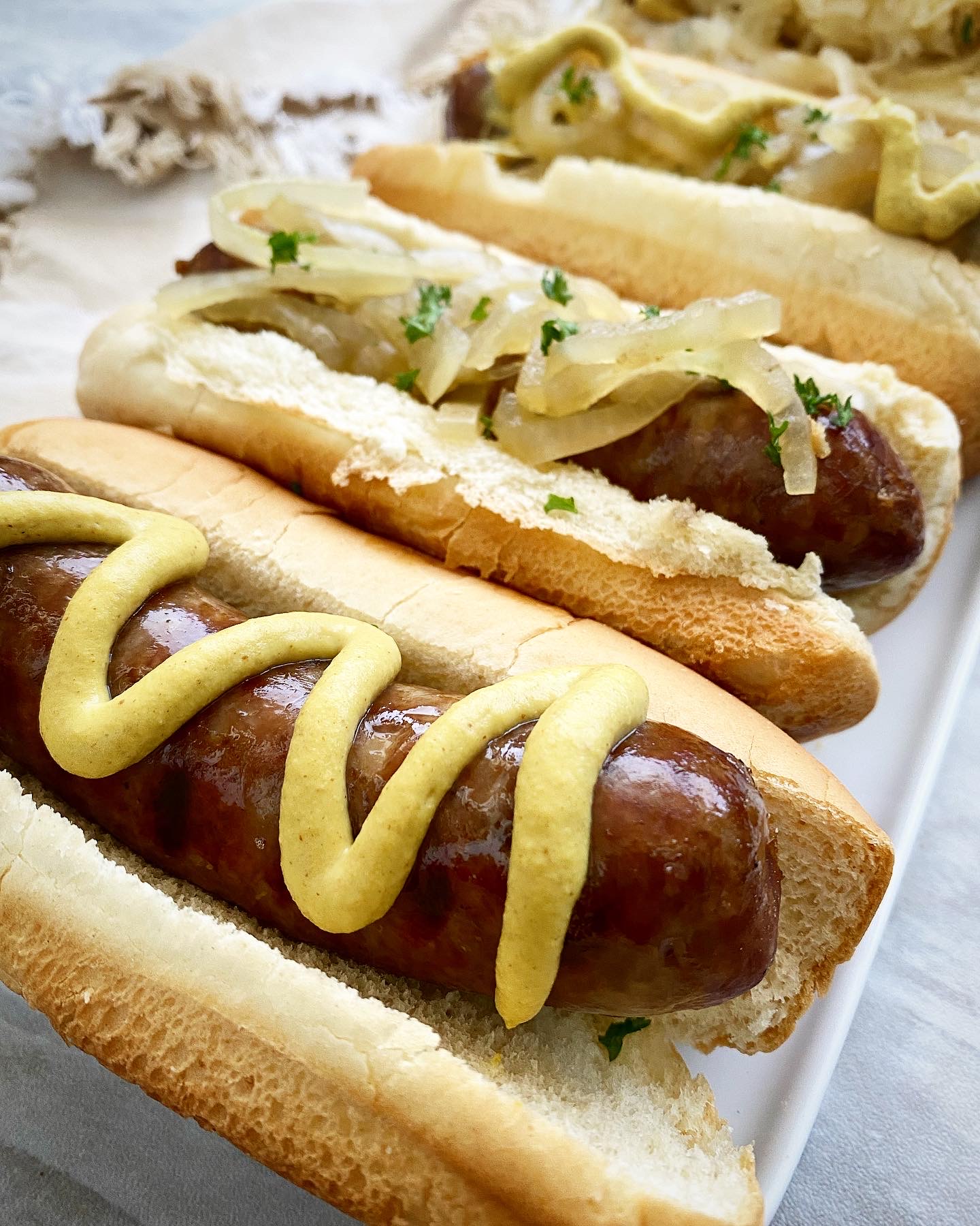 close up side view of beer brats in buns with condiments