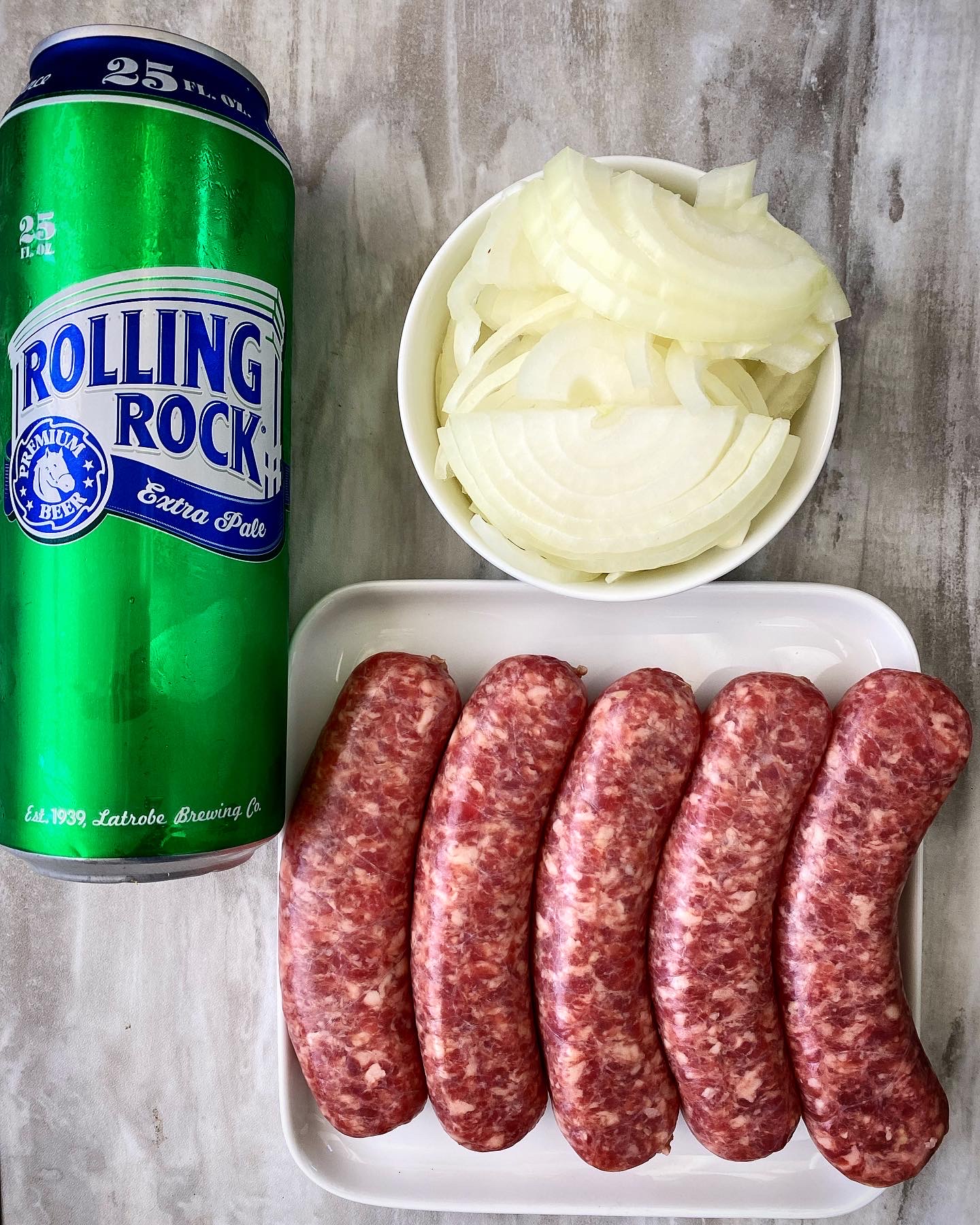 rolling rock, sliced onion in a bowl and brats on a white plate