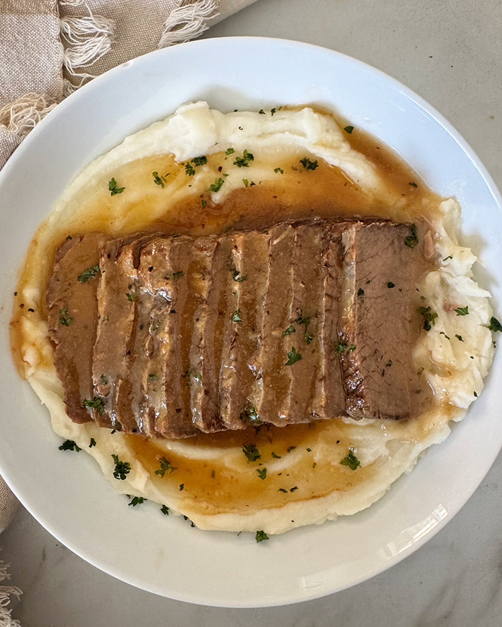 overhead shot of cooked brisket and gravy on a white plate