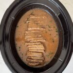 overhead shot of cooked brisket and gravy in a black slow cooker that has been sliced