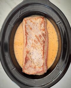 overhead shot of uncooked brisket and gravy in a black slow cooker