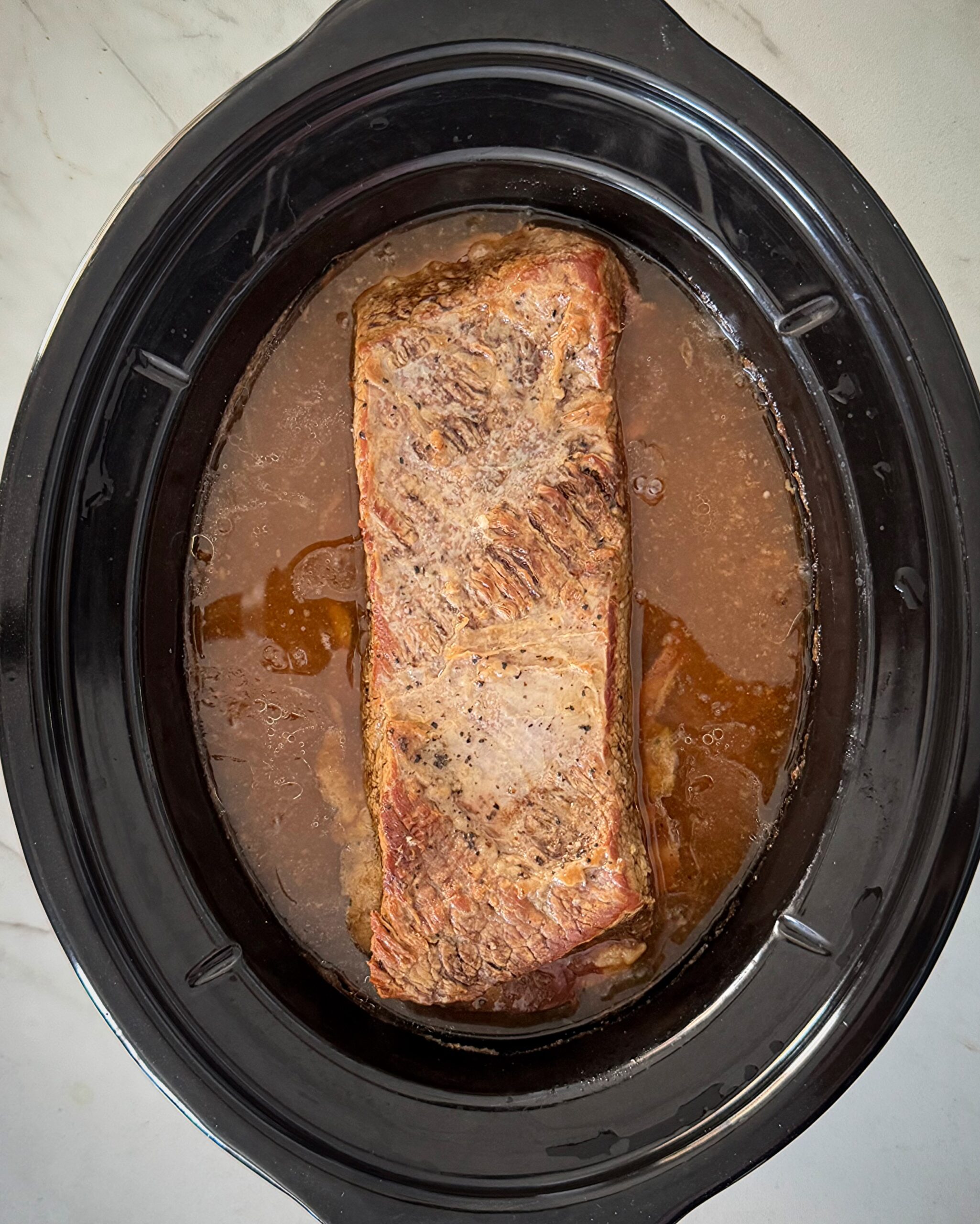 overhead shot of cooked brisket and gravy in a black slow cooker