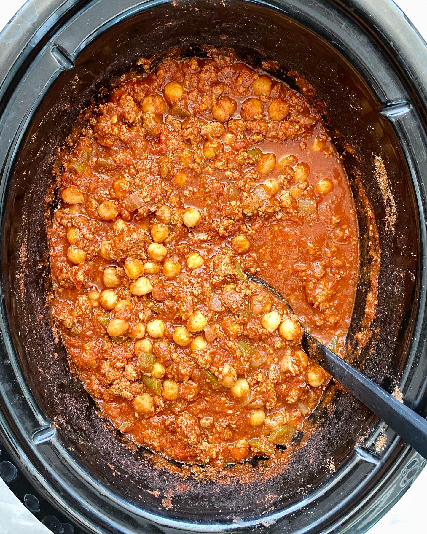 cooked indian spiced chili in a black slow cooker with a black spoon