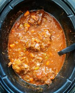 overhead shot of cooked oxtail stew in a black slow cooker