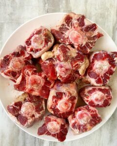 raw oxtails on a white plate seasoned with salt & pepper