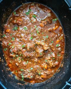 overhead shot of cooked oxtail stew in a black slow cooker garnished with parsley