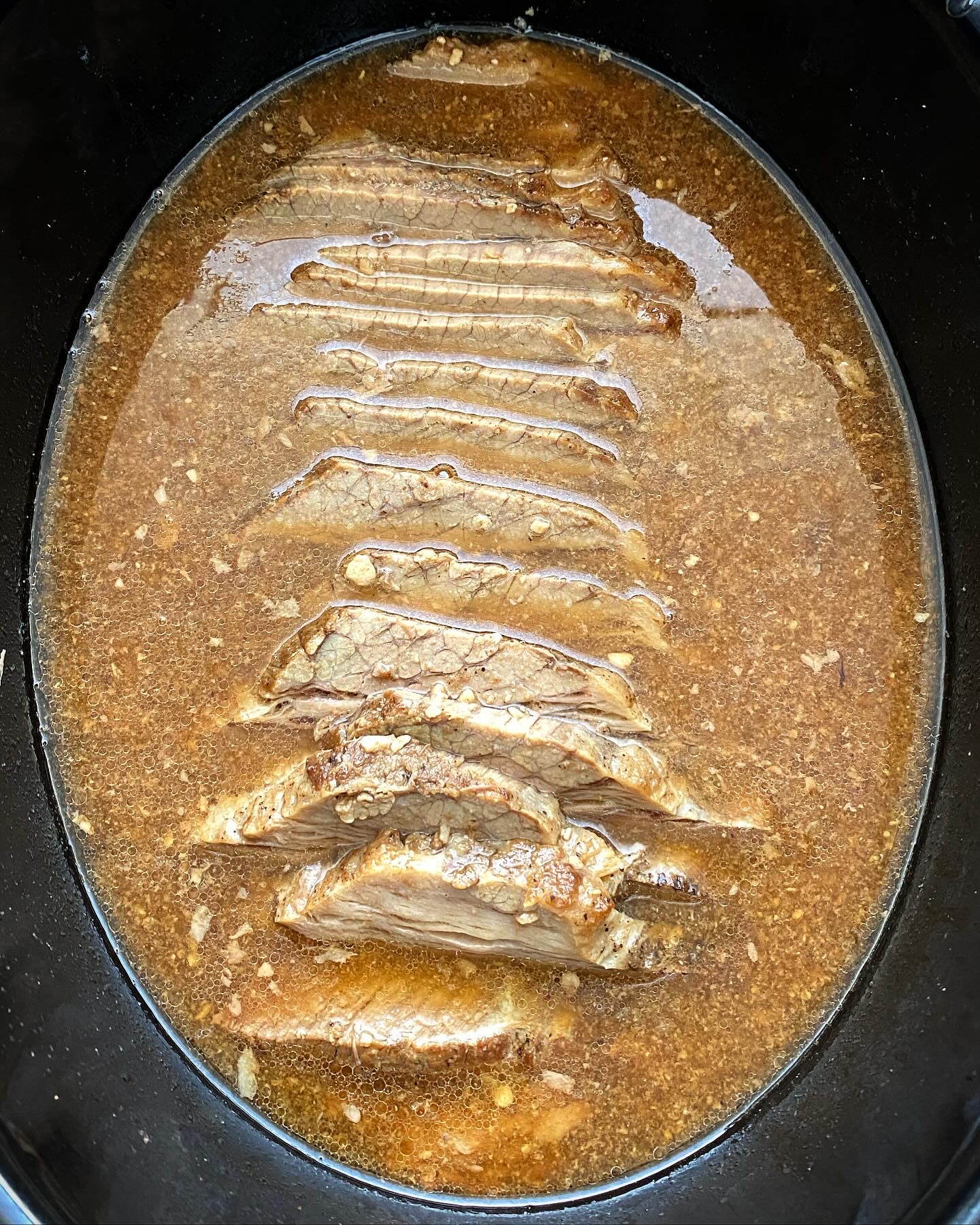 overhead shot of cooked, sliced brisket in a black slow cooker