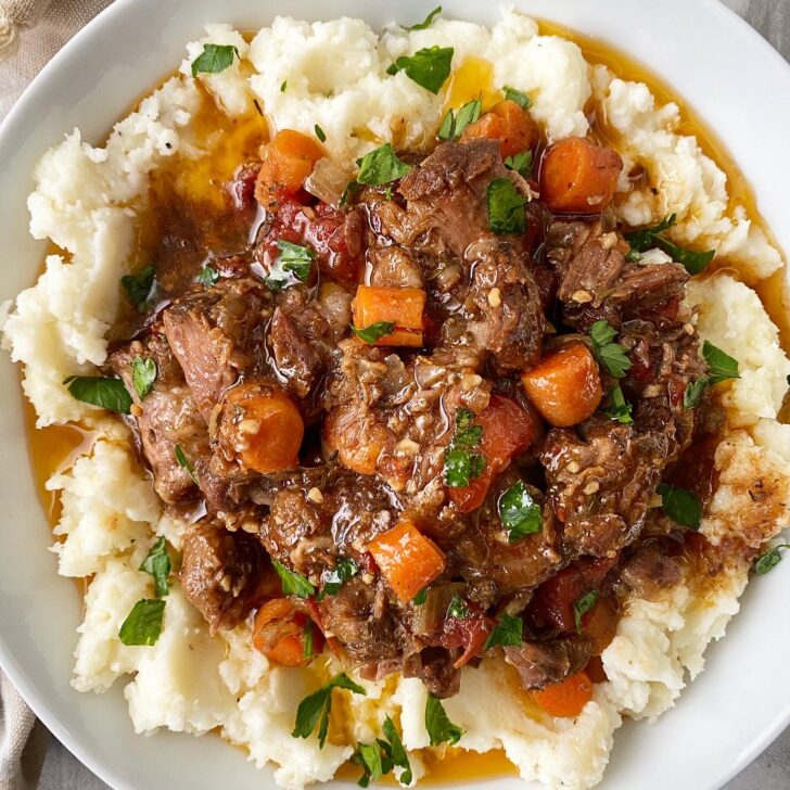 overhead shot of cooked oxtails on top of mashed potatoes in a white bowl