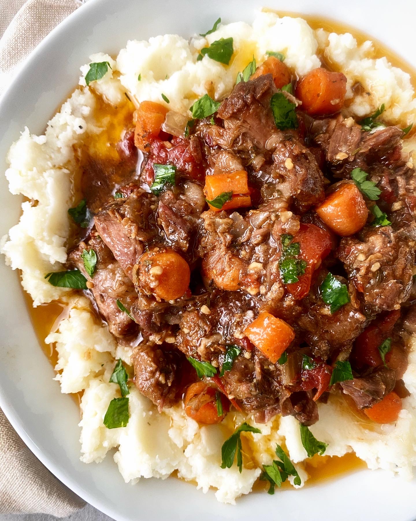 overhead shot of cooked oxtails on top of mashed potatoes in a white bowl