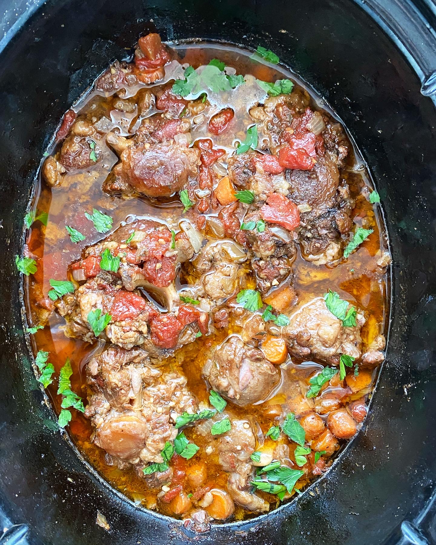 overhead shot of cooked oxtails in a black slow cooker