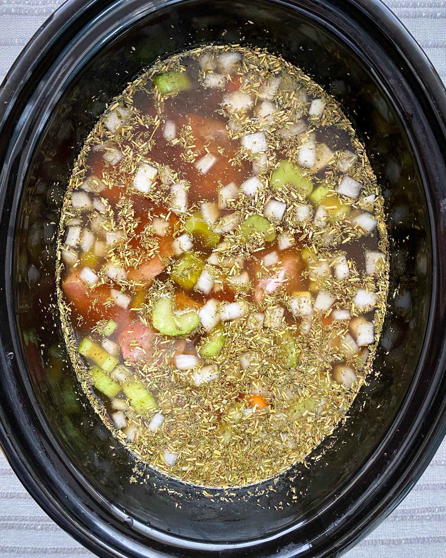 overhead shot of uncooked crockpot pot roast soup in a black slow cooker