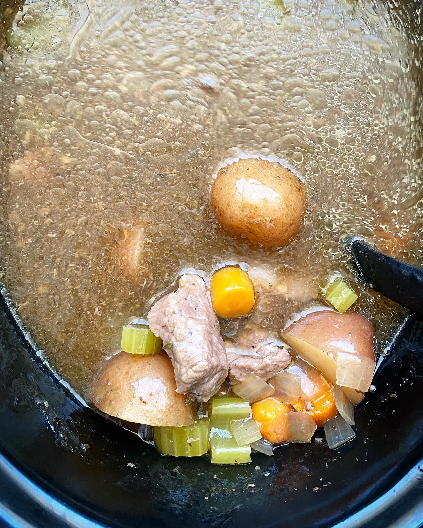 overhead shot of cooked crockpot pot roast soup in a black slow cooker