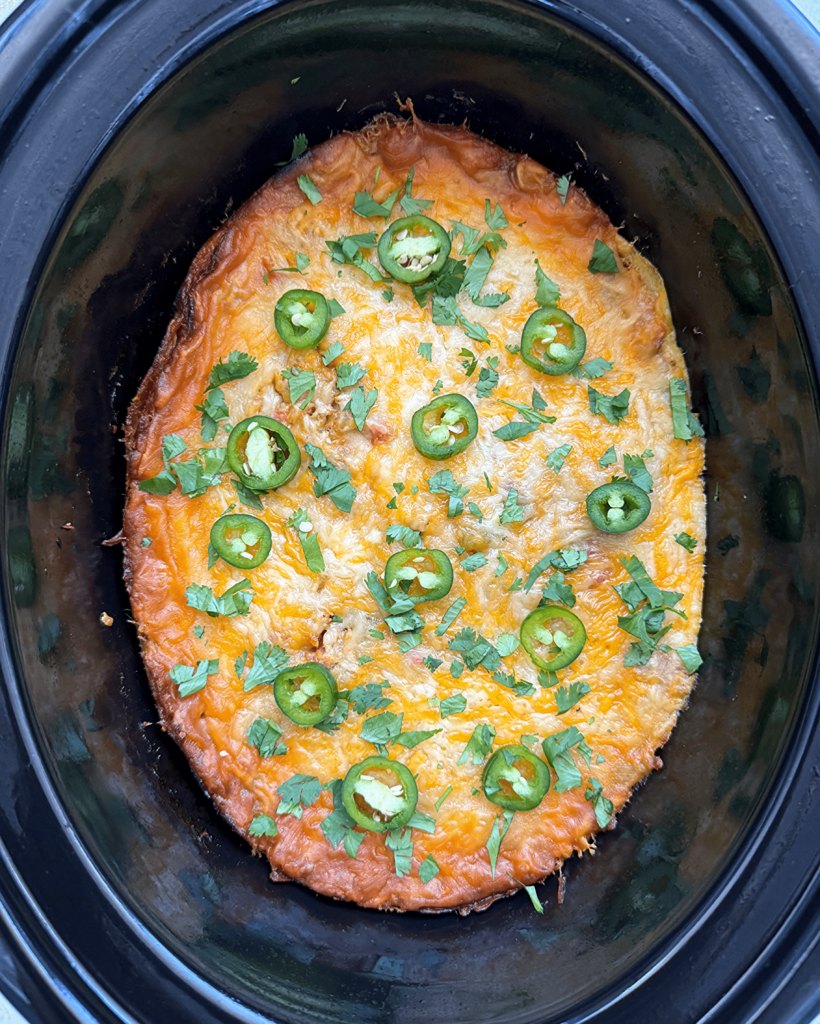 overhead shot of cooked salsa verde chicken casserole in a black slow cooker