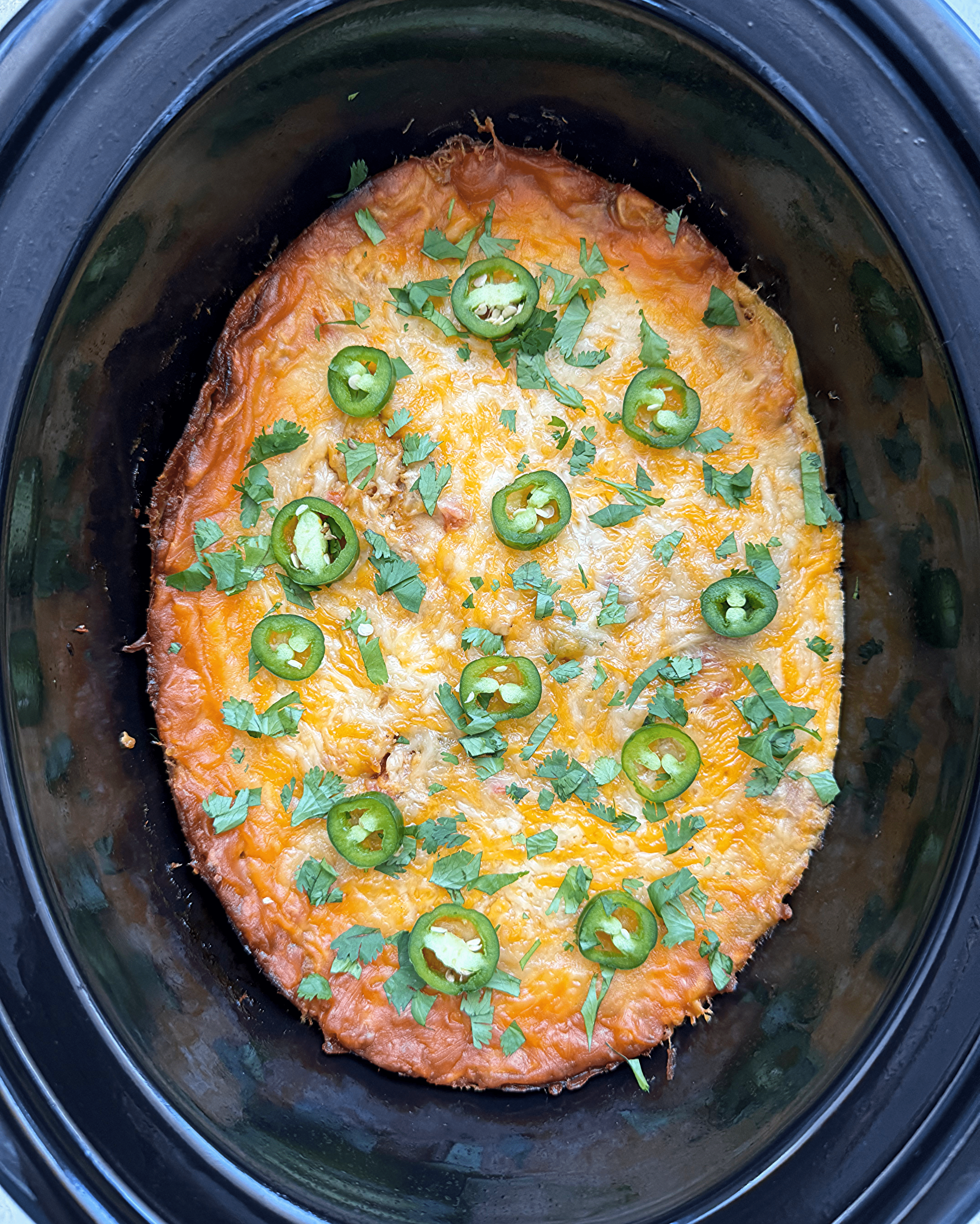 overhead shot of cooked salsa verde chicken casserole in a black slow cooker