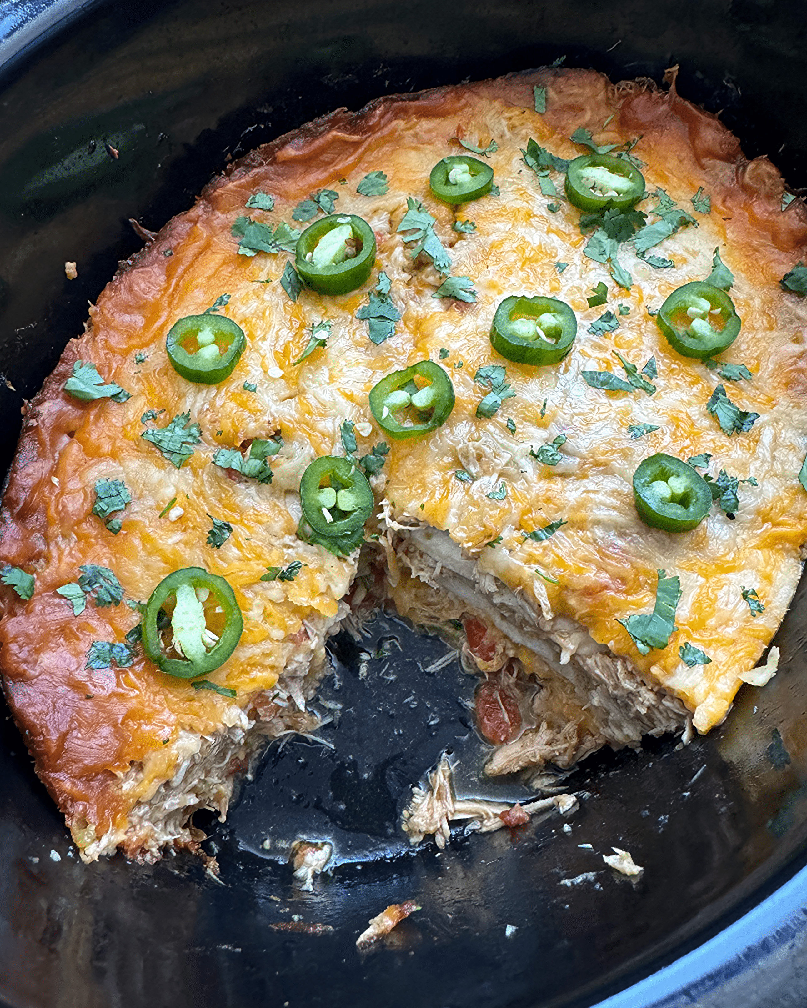 overhead shot of salsa verde chicken casserole in a black slow cooker with a chunk cut out the middle