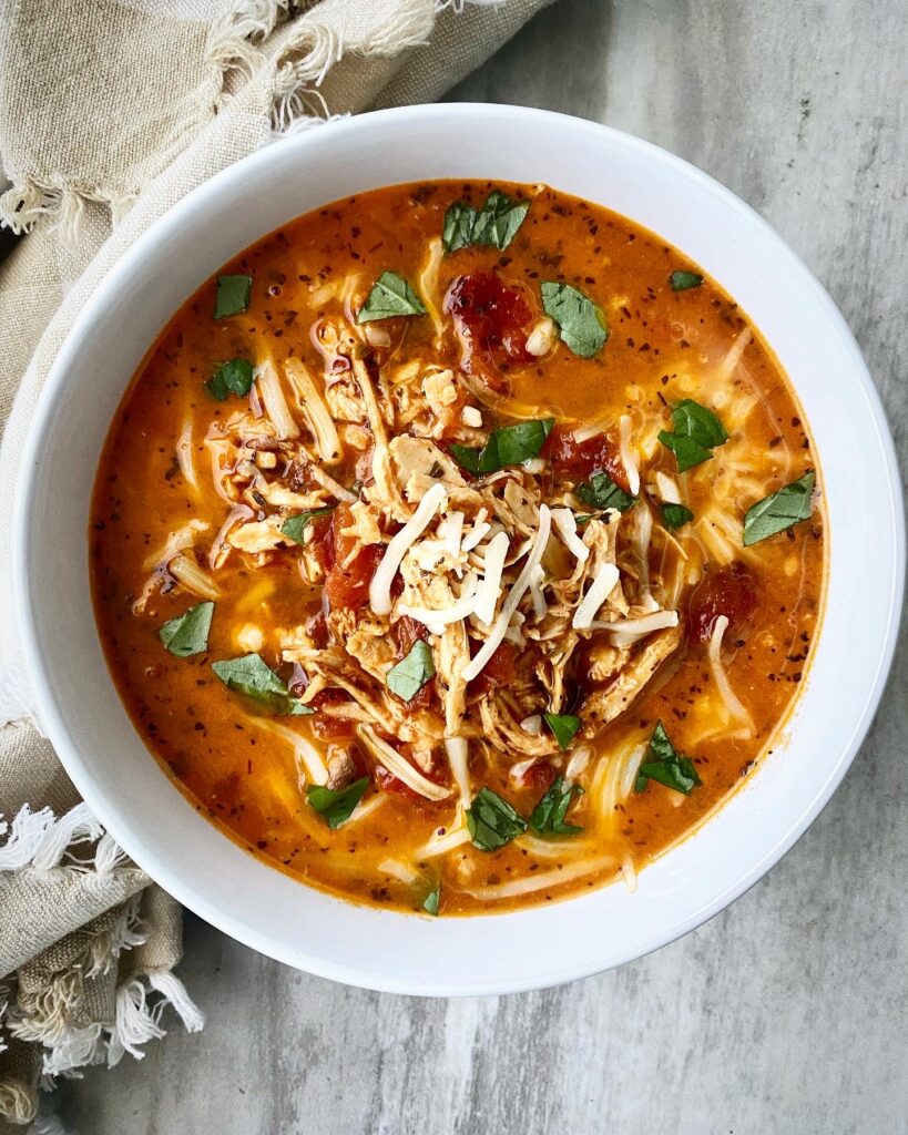 overhead shot of Caprese chicken stew in a white bowl garnished with fresh basil