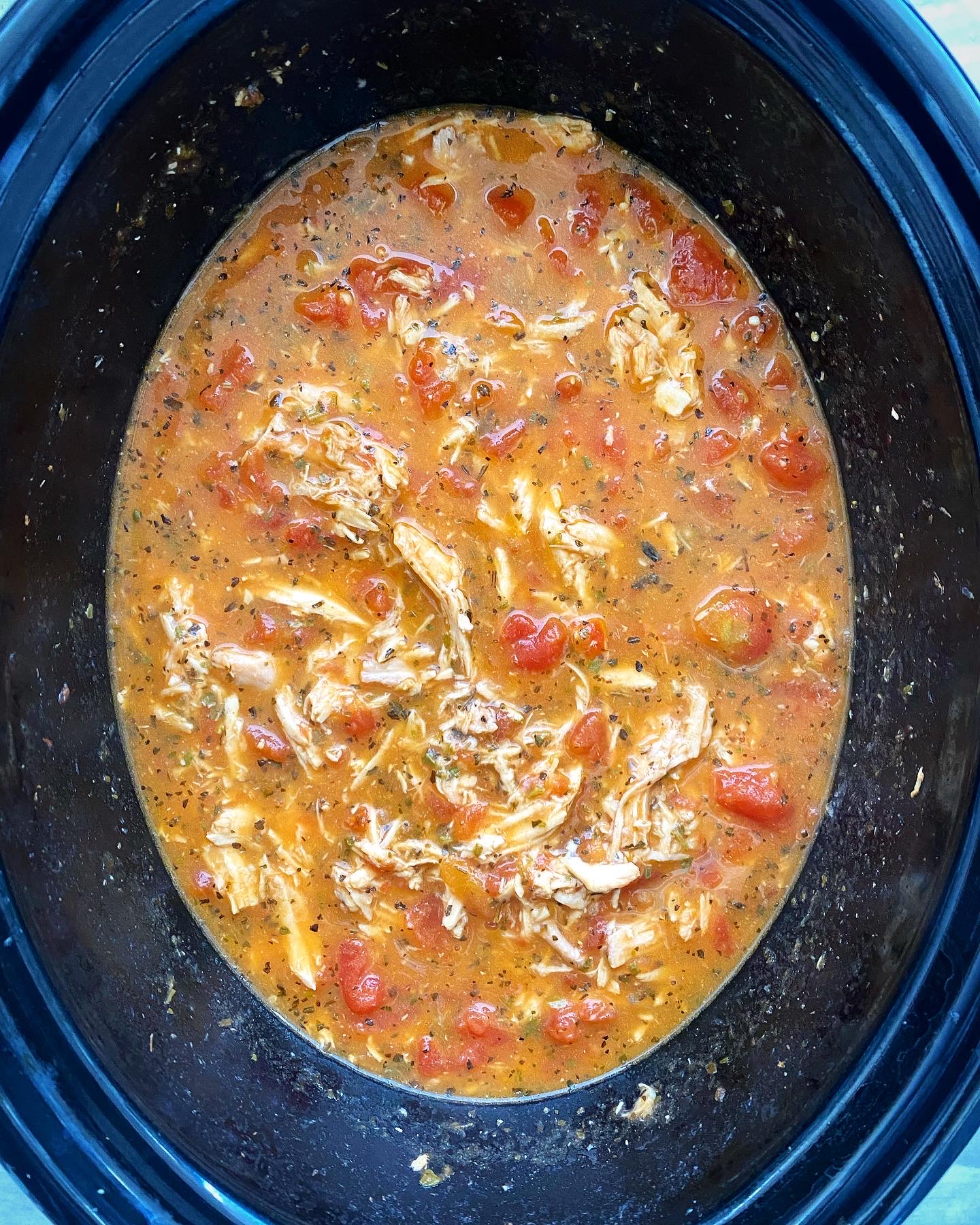 overhead shot of uncooked caprese chicken stew in a black crockpot