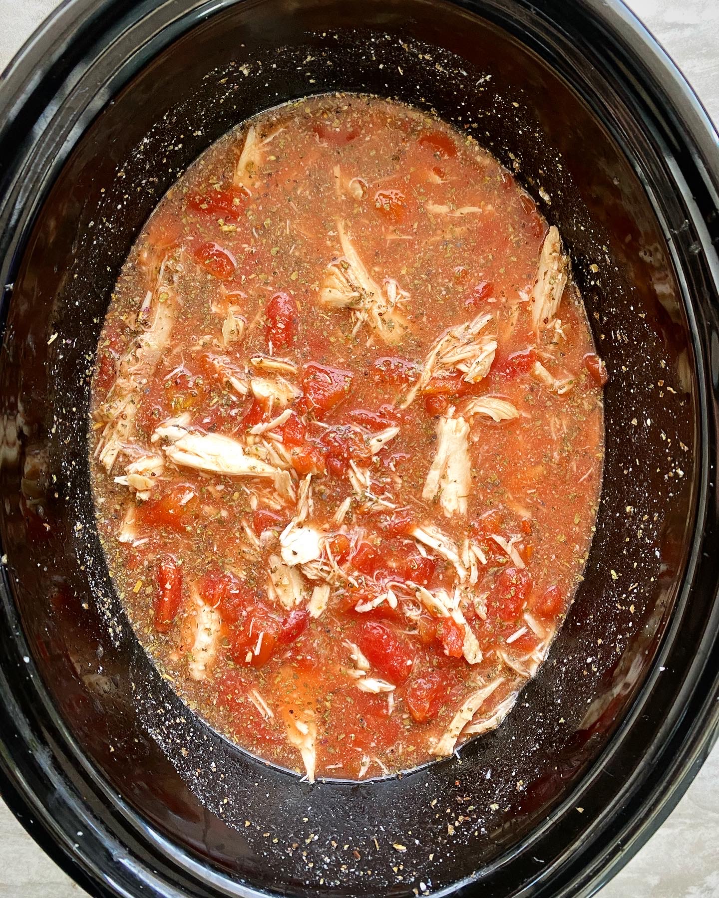 overhead shot of cooked caprese chicken stew in a black crockpot