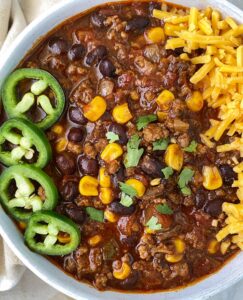 close up of chorizo beef chili in a white bowl garnished with sliced jalapeno, cheese and cilantro