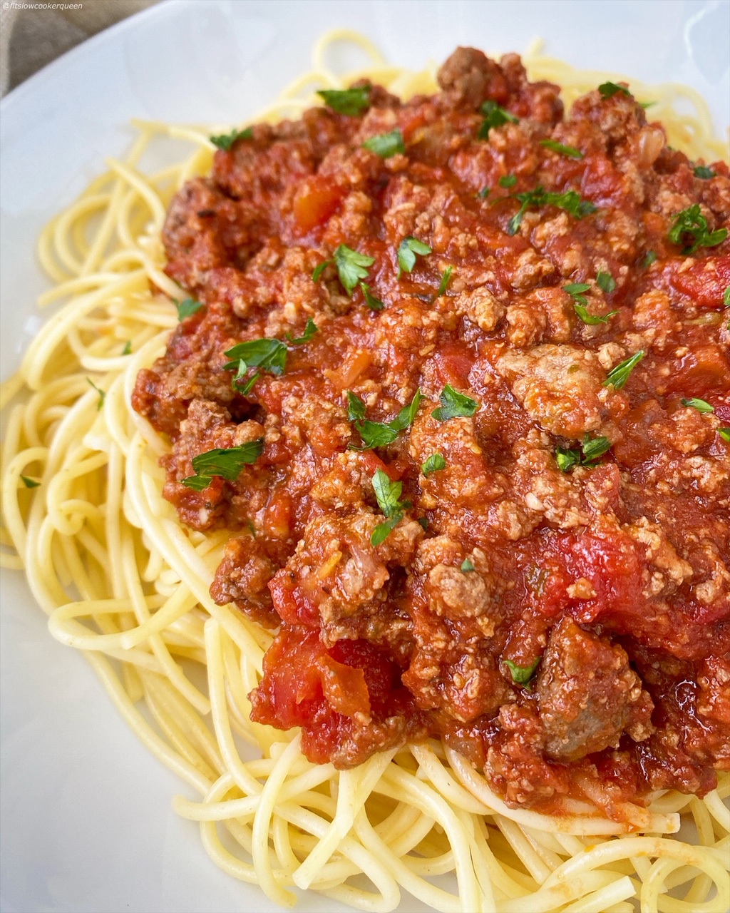 meat sauce over spaghetti noodles in a white bowl