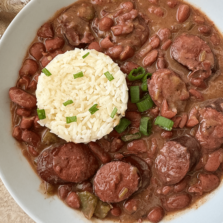overhead shot of red beans and smoked sausage in a white bowl with white rice