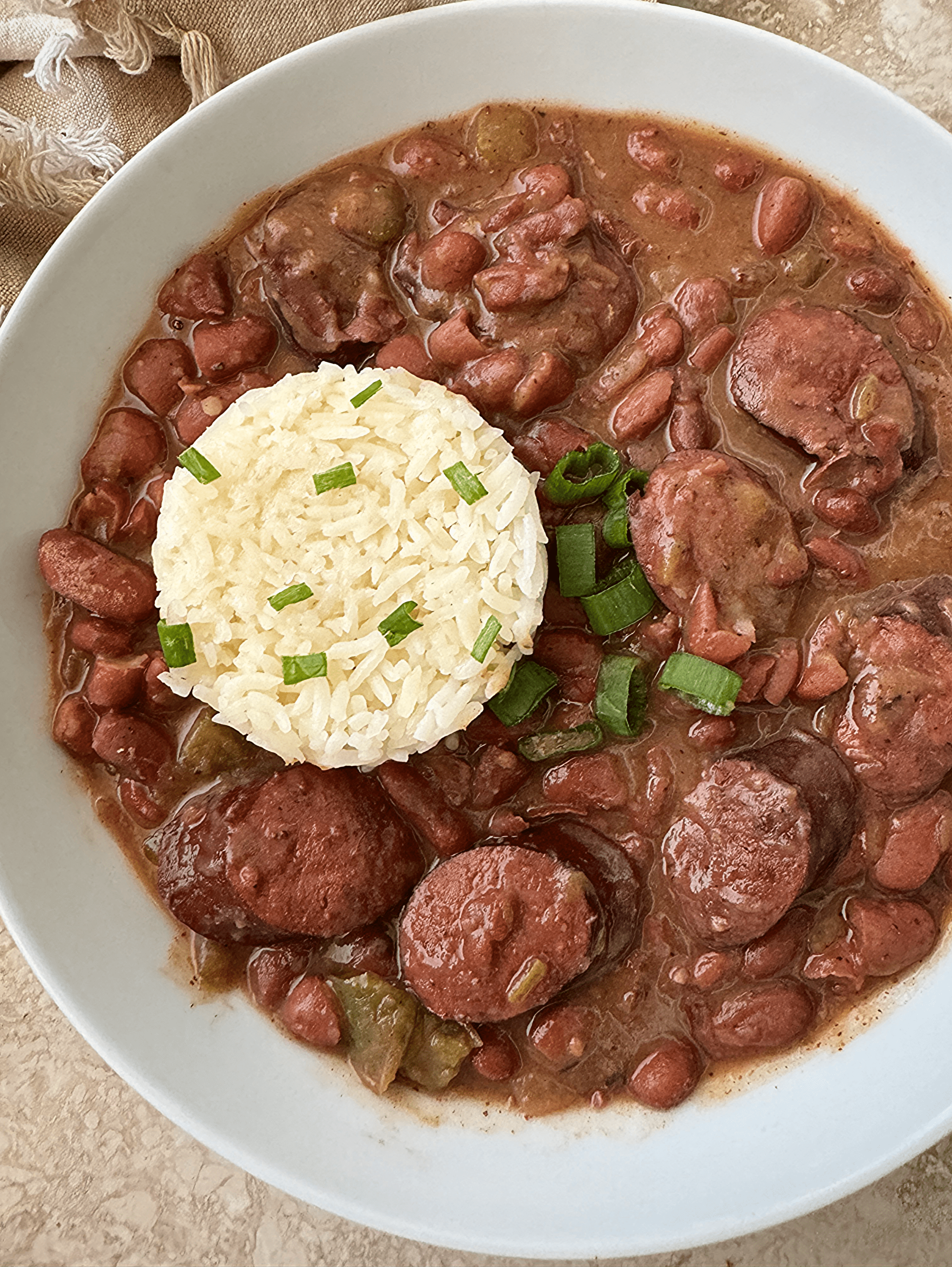 overhead shot of red beans and smoked sausage in a white bowl with white rice