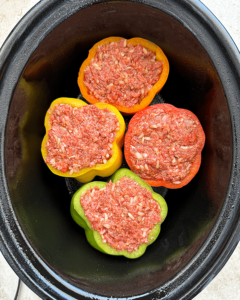 overhead shot of uncooked stuffed peppers in a black slow cooker