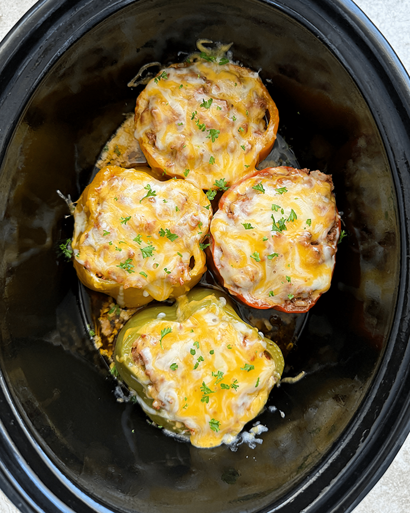 overhead shot of uncooked stuffed peppers in a black slow cooker with cheese