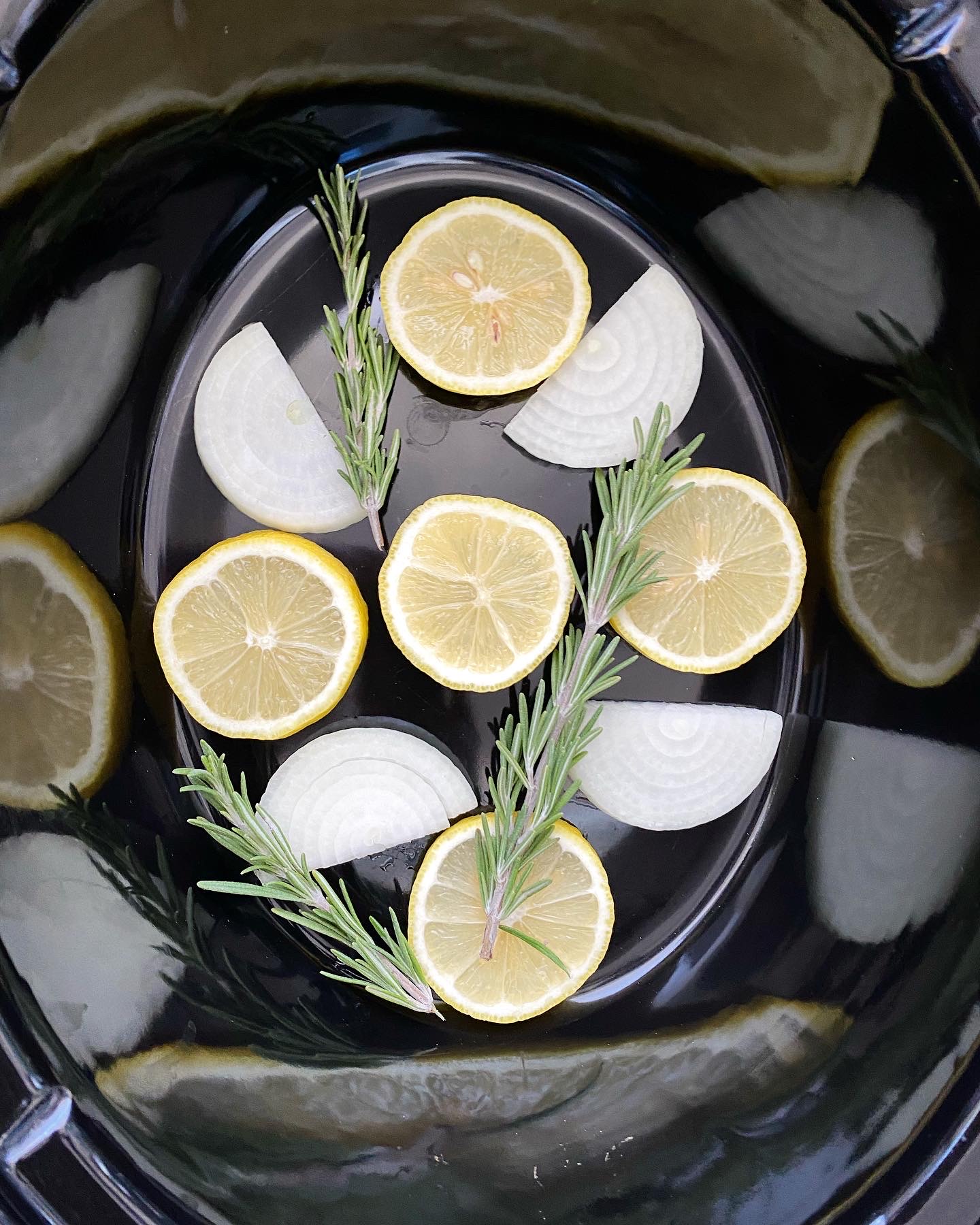 overhead shot of sliced lemon, onion, and sprigs of fresh rosemary in a black crockpot