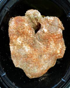 uncooked, seasoned turkey breast in a black crockpot