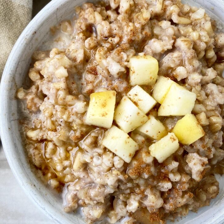 overhead shot side view of slow cooker apple cinnamon oatmeal in a white bowl with diced apple on top