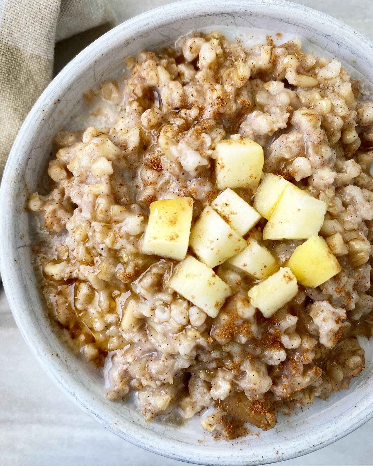 overhead shot side view of slow cooker apple cinnamon oatmeal in a white bowl with diced apple on top