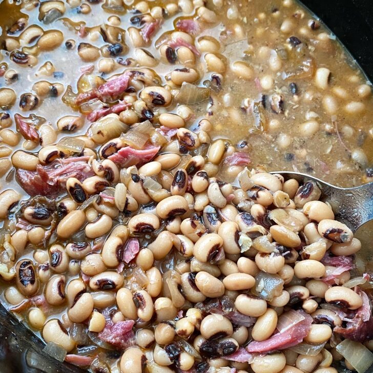 close up shot of cooked black-eyed peas with ham hock meat in a black slow cooker