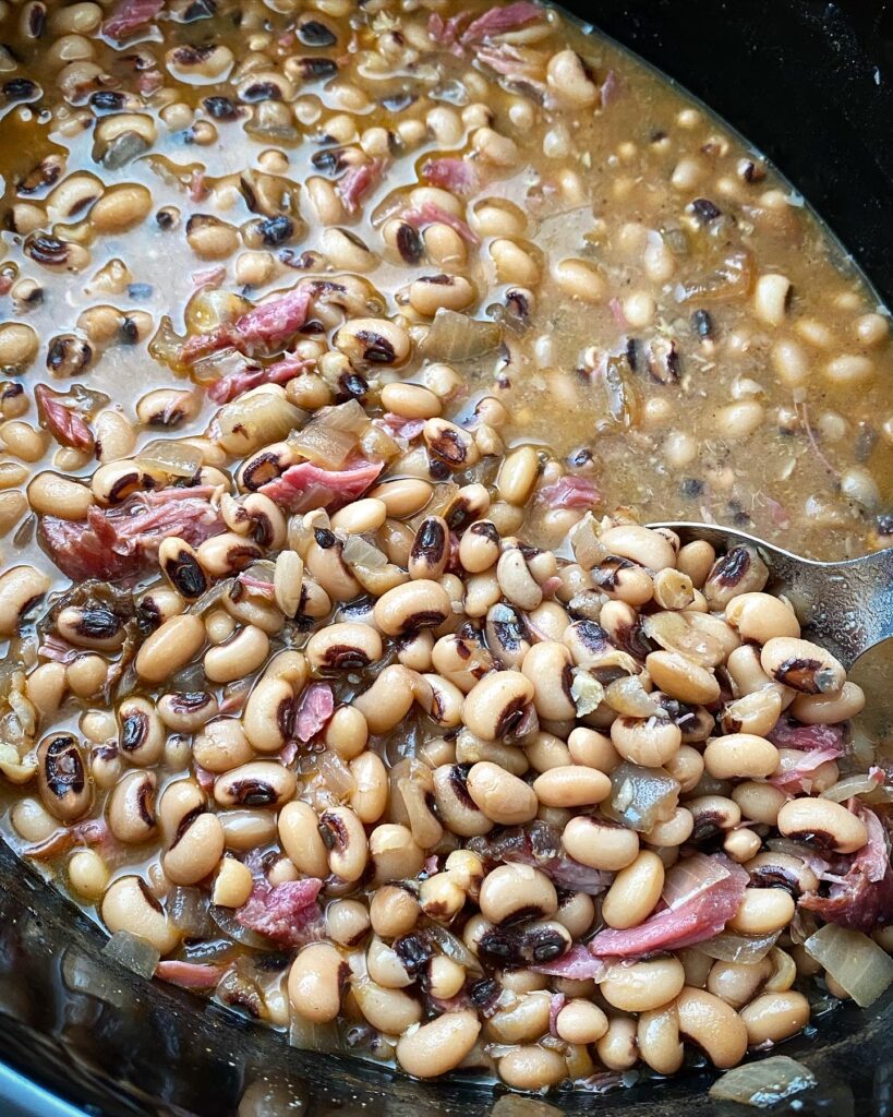 close up shot of cooked black-eyed peas with ham hock meat in a black slow cooker