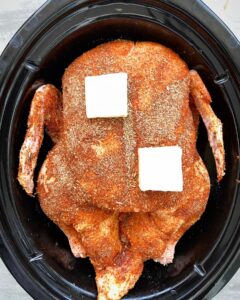 overhead shot of uncooked seasoned duck with butter on top in a black slow cooker