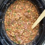 overhead shot of cooked black eyed peas and shredded beef in a black slow cooker