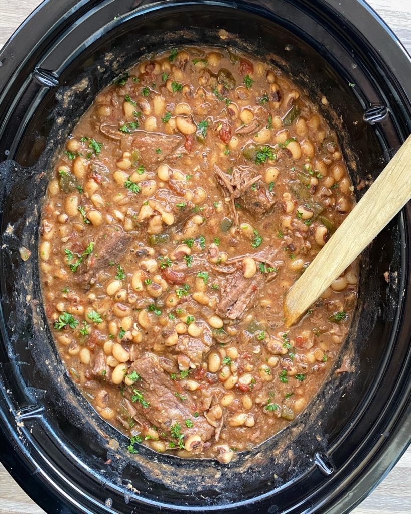 overhead shot of cooked black eyed peas and shredded beef in a black slow cooker