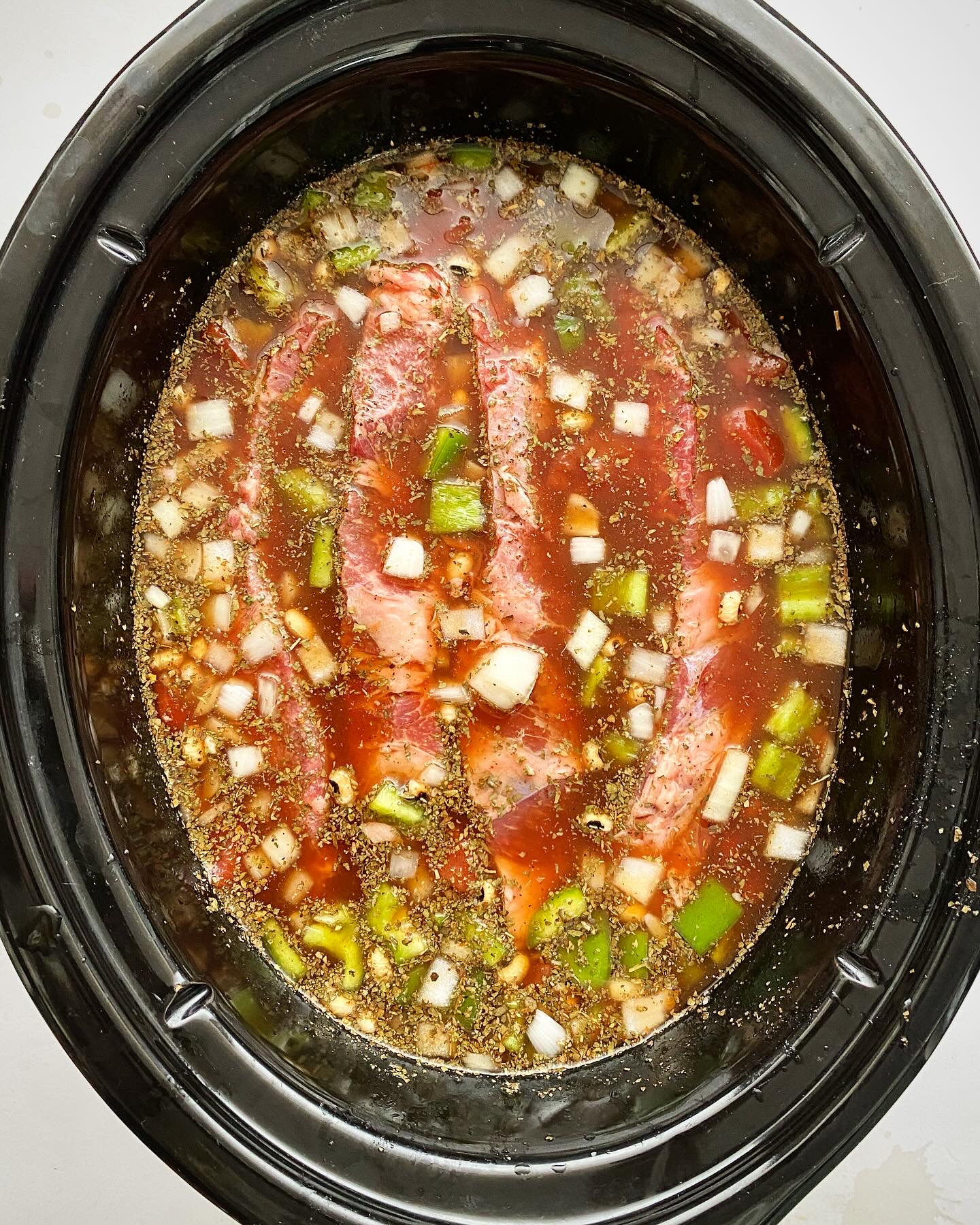 overhead shot of uncooked black eyed peas and beef in a black slow cooker