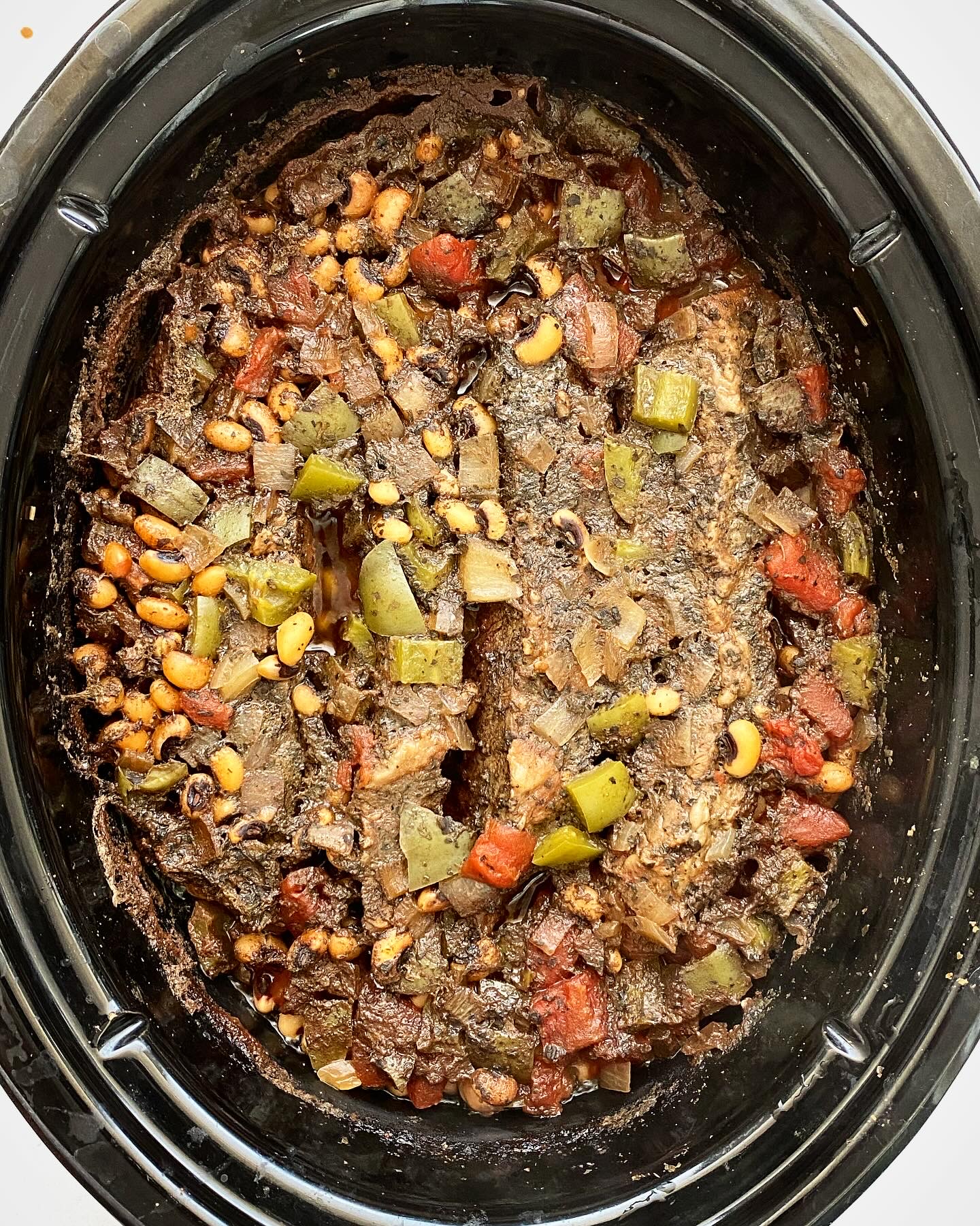 overhead shot of cooked black eyed peas and beef in a black slow cooker