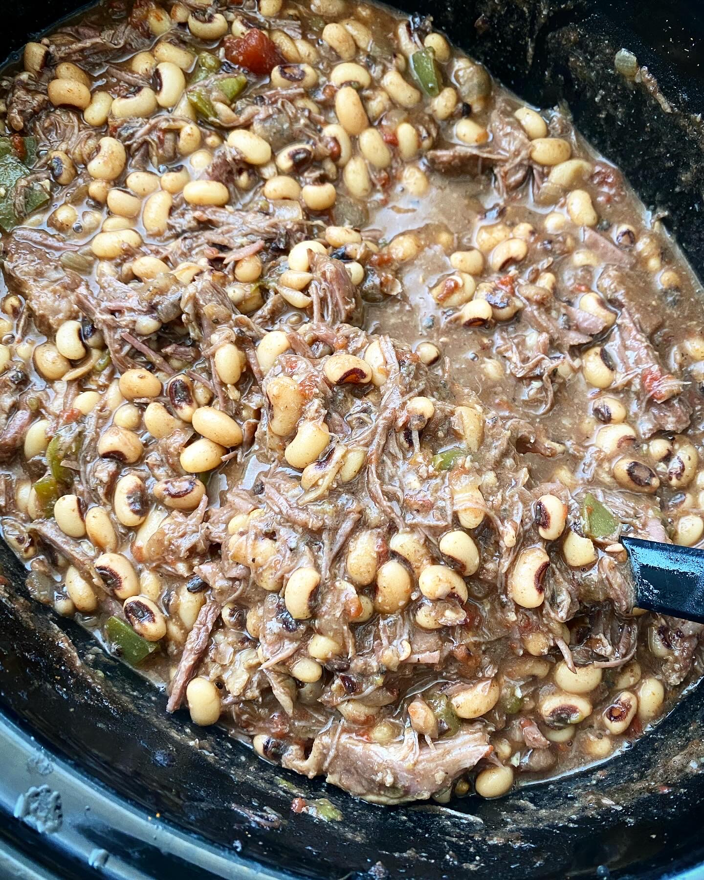 overhead shot of cooked black eyed peas and shredded beef in a black slow cooker