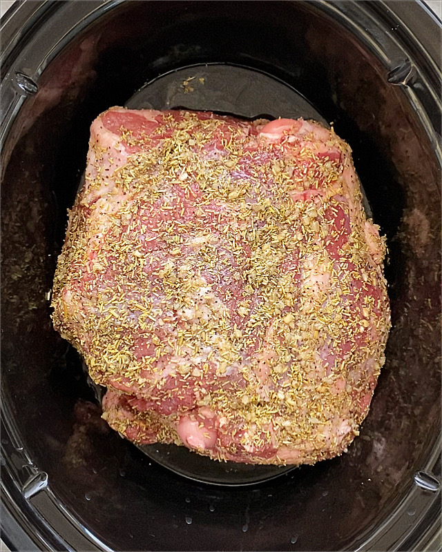 overhead shot of uncooked leg of lamb in a black slow cooker
