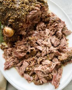 overhead shot of cooked leg of lamb on a white platter, half shredded