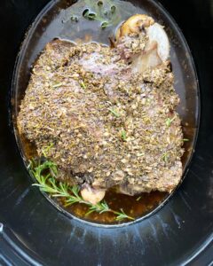overhead shot of cooked leg of lamb in a black slow cooker