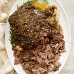 overhead shot of cooked leg of lamb on a white platter, half shredded