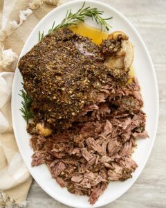 overhead shot of cooked leg of lamb on a white platter, half shredded