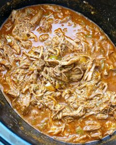 close up shot of enchilada shredded tri-tip in a black slow cooker