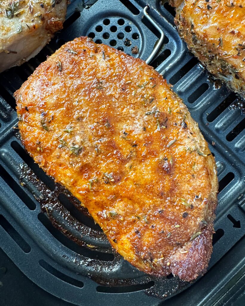 close up shot of 1 cooked pork chop in a black air fryer