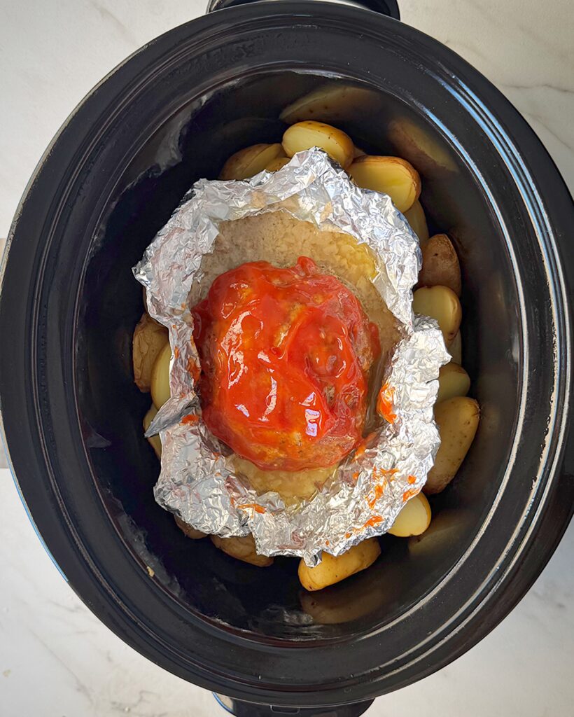overhead shot of cooked meatloaf and potatoes in a black slow cooker